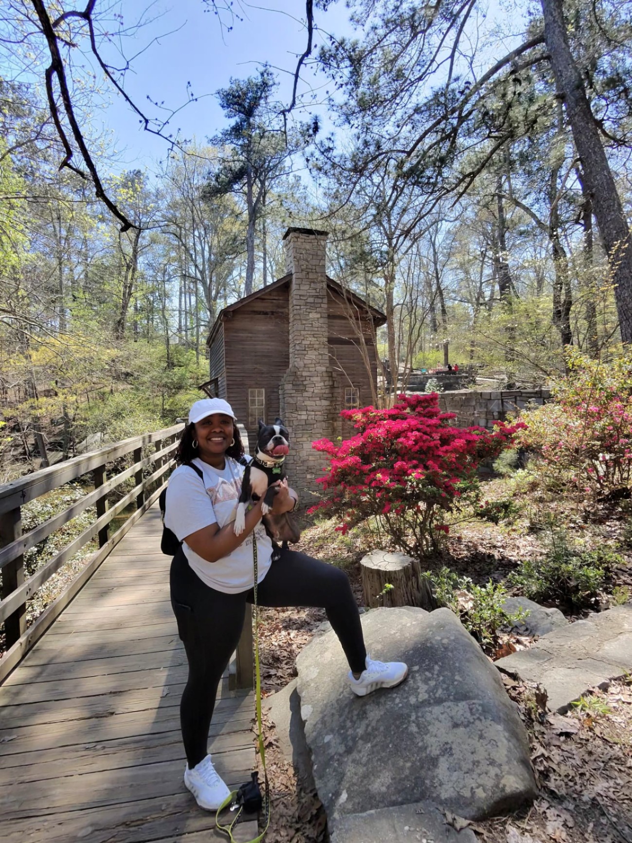 Ashley Catan hiking with her dog in a wooded park near a historic stone cabin.